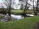 Square grassed area surrounded by moat and some trees with a wooden bridge