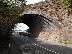 A stone arch spanning a narrow road at an oblique angle