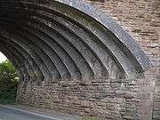 From a wall of stone, 13 narrow blue brick arch ribs spring. The spandrel wall, above, is also made of stone.