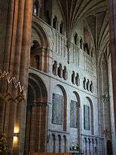  A transept interior with a wall panelled with shallow Norman arches and open galleries.
