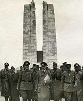 A group of men dressed in Nazi German soldier, front and centre is Adolf Hitler. The twin pylons of the memorial are clearly displayed in the background.