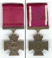The obverse and reverse of the bronze cross pattée medal; obverse showing the crown of Saint Edward surmounted by a lion with the inscription FOR VALOUR with a crimson ribbon; the reverse shows the inscription of the recipient on the bar connecting the ribbon with the regiment in the centre of the medal.