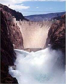 Front view of a dam in a narrow canyon, with water shooting out of the gates