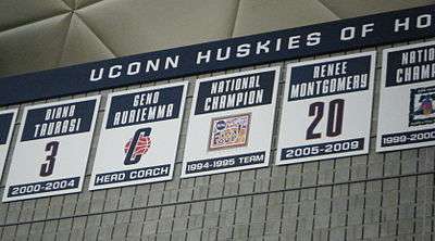 Gray stone wall with five placards attached in a row, with numbers or logos on them. Above is a triangular-grid ceiling.