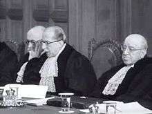 Three men in judge's robes seated at a bench, the middle one speaking