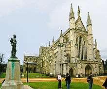 This exterior view at Winchester, taken from near the north west corner of the cathedral, and with a war memorial statue in the foreground, looks acutely along the north side of the building, showing it receding into the distance.