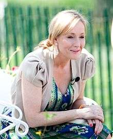 J. K. Rowling, author of Harry Potter and the Half-Blood Prince, crouches. She is wearing a blue dress under a grey jacket.