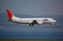 A Boeing 737-400 aircraft painted in new JAL corporate livery with a skyline background