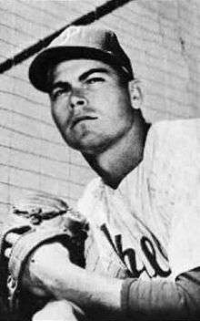 A black-and-white photograph of a man wearing a white baseball jersey with "Phillies" (obscured) across the chest, a dark-colored baseball cap with a white "P" on the front, and a baseball mitt on his left hand