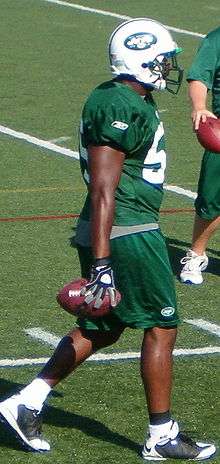African American male in green jersey and white helmet holding a football