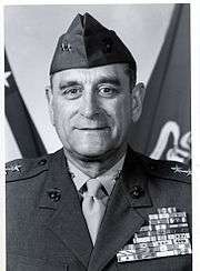 Head and shoulders of a middle-aged white man with a subdued smile wearing a garrison cap with two stars on either side and a military jacket with a large array of ribbon bars covering the entire left breast.