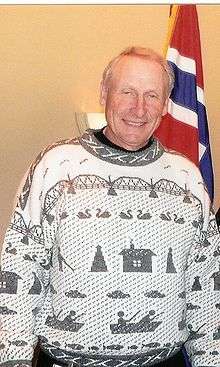 Man in light gray winter style sweater standing in front of Norwegian flag