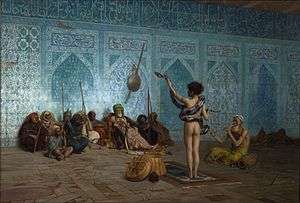 This painting shows the back side of a naked man standing with a snake wrapped around his waist and shoulders. The man is lifting up the head of the snake with his left hand. Another man to his right is sitting on the ground playing a pipe. A group of 10 men are sitting on the floor facing the snake handler with their backs against an ornate blue mosaic wall decorated with Arabic calligraphy.