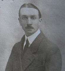 A mid-length portrait of a man of about 30 in a conservative suit and wearing a moustache, facing the camera.