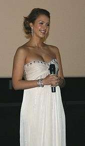 Smiling young woman in strapless white dress, holding a microphone.