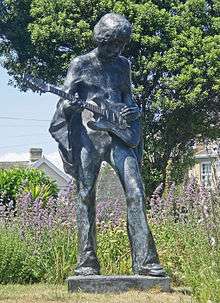 A color photograph of a bronze statue of a man holding an electric guitar.