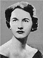 A black and white photograph of a formally dressed woman with short, dark hair