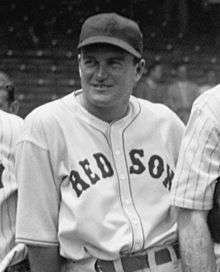 A smiling man wearing a white baseball uniform with "RED SOX" across the chest and a dark baseball cap