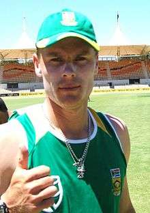 A white coloured man wearing a green cap and T-shirt and giving a thumbs-up.