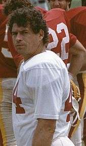 An American football player looks to his left in the direction of the camera. He is not wearing his helmet.