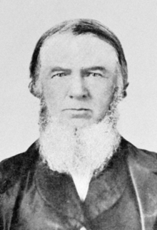 Black and white photograph of John Baker White, who has a beard and is wearing a suit.