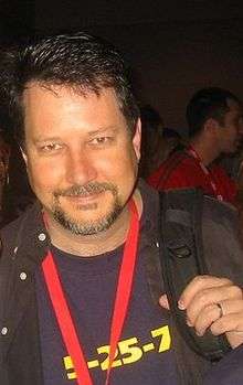 A man in his forties is seen wearing a backpack and a red necklace.