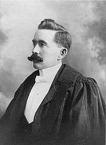A formal portrait of a left-facing man with a moustache, wearing barrister's robes