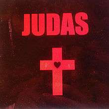 The word "Judas" is written in capital red letters on a dark brown background. Below is a red cross with a black heart in the middle.