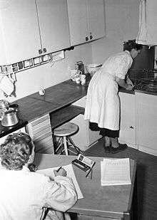 En kvinna arbetar i köket, en annan kvinna antecknar och klockar tiden (Rålambsvägen 8 och 10 i Stockholm)