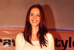 Koechlin in a white dress smiling at the camera