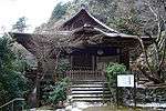 Frontal view of a wooden building with white walls and undulating gable in line with the eaves and below a normal gable.