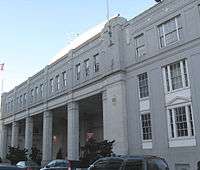 Facade of a large white building, the left having large pillars beneath a strip with dozens of windows and the right three stories of large windows.