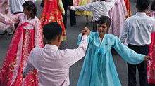 Women dressed in traditional outfits dance with men on the street.