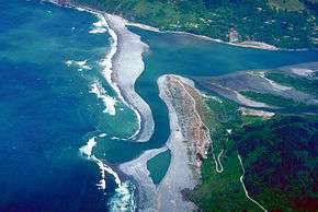 Aerial view of the river flowing between peninsulas of sand and into the ocean, which is the same color as the river water