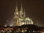 A large, brightly lit cathedral sits in the middle of a skyline at night.