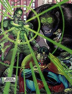 A robotic man with a green glow coming from his chest. Superman on his knees, sick and bleeing. A huge gorilla stands in the background.