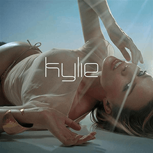 An image of a woman lying down on a marble-like surface, wearing a tan-coloured bikini. The title "Kylie" is superimposed on her.