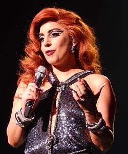 Lady Gaga is holding a mic in her right hand.