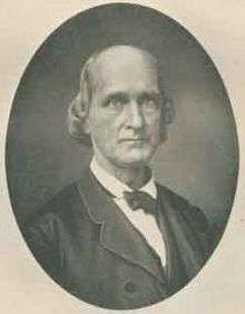 A balding, clean-shaven man, facing right. He is wearing a white shirt, black bow tie, and black jacket