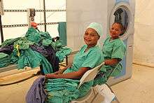 Two women with large piles of scrubs and a washing machine