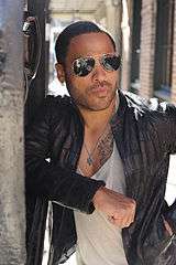 A colored photograph of Lenny Kravitz, wearing sunglasses and a black jacket.