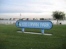 A blue sign stands in the middle of a park. "Leo J. Ryan Park" is written on it.