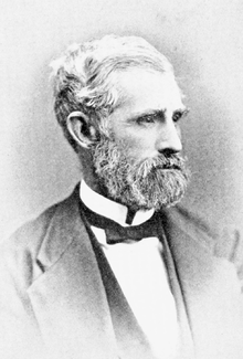 Head and shoulders photograph of a man in a Victorian suit.  He has a white beard and large mustache  He wears a serious expression and is looking to the left.