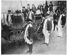 A large bell is seen tied to a wagon. Soldiers in Revolutionary War uniforms stand by.