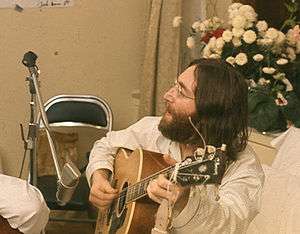 Colour photograph of John Lennon playing an acoustic guitar.