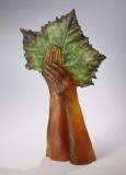 Amber glass hands hold up a green cast glass leaf