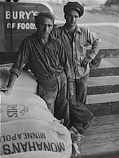 Two men who loaded flour and a bag of flour that says Monahan's Minneapolis and a Pillsbury truck