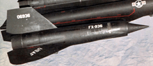 A part of a black, delta-winged aircraft with engine nacelle partway out the wing; U.S. Air Force insignia on the fuselage, "USAF" labeling on the wing, and "FX-936" coding on the nacelle