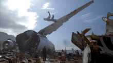A large amount of airplane debris surrounds people on a beach.