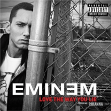 A monochrome still of Eminem, leaning on a perimeter fence to the right.
